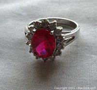 Front view of sterling silver ring showing oval pink red facetted central stone surrounded by clear cubic zirconia stones.
