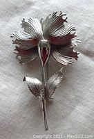 Front view of vintage sterling silver flower brooch showing detailed petals and two leaves on stem.