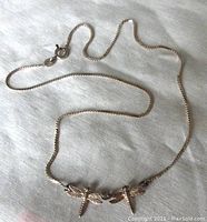 Full view of silver chain necklace with two dragonfly pendants arranged on fabric.