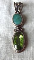 Front view of pendant showing facetted green peridot and smooth green emerald stones set in sterling silver with fancy bail.