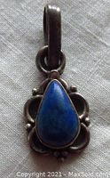 Front view of vintage sterling silver pendant with pear-shaped lapis lazuli stone on white fabric background showing darkened silver details.