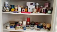 Wide view of various candles and candle holders on shelf including pillar, taper, votive, and gel candles with metal holders