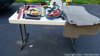 Photo showing table with assorted car tools, jumper cables, dog accessories, and two Honda CRV car rugs hanging on side of table