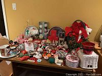 Wide view of Christmas decoration lot including ornaments, ribbons, baskets, mugs, candles, trays, and lights arranged on wooden table