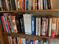 Shelf with various cookbooks, some hardcover, some spiral-bound, including numerous recipe collections.