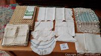 Top view of assorted embroidered doilies, napkins, placemats, tablecloth laid out on surface.