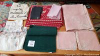 Tablecloth, assorted napkins, aprons, and placemats arranged on a wooden surface showing various textiles.