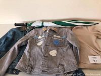 Three jackets arranged flat including medium fleece, large blue denim, and medium grey denim with appliqués, plus a folded umbrella.