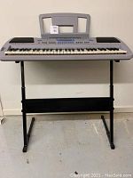 Front view of electronic keyboard mounted on black metal stand, placed against wall.