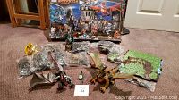 Photo showing all loose and bagged pieces including dragon figures, warrior mini-figures, accessories, and castle parts arranged on floor with original box in background