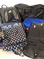 Group photo of multiple bags including the Nike backpack, Vera Bradley hanging toiletries bag and wristlet, leather tie travel case, and various duffle and travel bags.