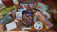 Wide shot showing Nintendo Wii console, controllers, sensor bar, adapter, two Wii games, and multiple board games and puzzles arranged on carpet.