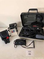 Polaroid camera with film pack, Nikon camera, Minolta Movie Master video camera in case, cables, film canisters, and black camera case.
