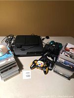 Overview of two consoles, six controllers, stacked game cases, cables on table