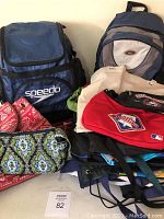 Front view of the lot showing Speedo backpack, Vera Bradley purse, other backpacks, fanny pack, and various bags arranged on the floor.