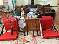 Two red stadium chairs, four racquets, one baseball bat, one softball, and black boxing gloves displayed on carpeted floor.