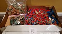 Photo showing a large quantity of mixed colored plastic toy army men in a box, including some in resealable plastic bags.
