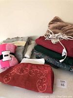 Bedding and throw items stacked including the pink Victoria's Secret throw, red Sunbeam electric throw, green fleece blanket, decorative pillow covers, and fuzzy brown pillow.