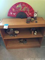 Wooden bookshelf with items including red handheld fan, decorative doll, braided basket, trinket boxes, and nesting doll