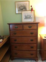 Full view of wooden dresser with six drawers and two framed floral prints resting on top plus glass fish bottle vase holding a faux rose.