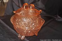 Front angled view of the amber-colored candy dish showing lovebird design on the lid, pressed glass patterns, and curled feet.