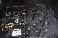 Lot of 19 bracelets arranged on black backdrop showing variety in materials and styles including black, wooden, metal, and beaded pieces