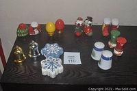 Photo showing 8 sets of Christmas holiday salt and pepper shakers arranged on dark wood surface, showing diverse designs including snowflakes, bells, snowmen, and hats.