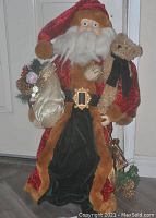 Front view of Santa figurine showing fur accented velvet outfit, fiber beard, gold sack of toys and teddy bear in arms