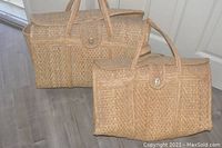 Two matching rattan woven tote bags placed on floor near white wall, showing overall shape and flap closure details