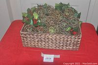 Photo of gold filigree balls and holly berry garland arranged inside the Tommy Bahama basket on a red table.