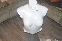 White female bust mannequin on metal stand on wood floor in front of couch
