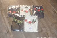 Five packaged blouses laid flat on a floor, showing assorted colors and sizes with poinsettia embroidery visible through packaging.