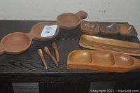 Photo showing all wooden serving pieces including three triple-section servers, three spoons, and one platter on a dark surface.