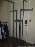 Black rectangular professional rolling clothing rack with 4 adjustable height arms, all removable, standing indoors near a door.