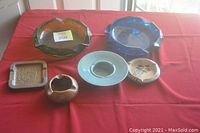 Photo showing six vintage ashtrays including large cobalt blue and avocado green glass ashtrays, and four smaller ashtrays in ceramic and wood.