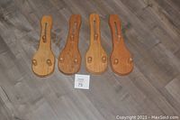 Four wooden plate display mounts aligned on floor, showing front view with rounded base and adjustable support pegs.