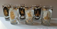 Front view showing all 8 glasses upright in a row displaying gold historical motifs on glass surfaces.