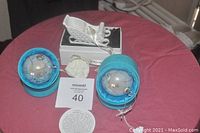 Photo of the three ornaments including the Pandora sleigh on its box and two LI BIEN dove glass ball ornaments in aqua-colored gift boxes placed on a red surface with MaxSold lot number and tag.