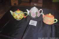 Three decorative ceramic teapots displayed on black surface, showing various designs.
