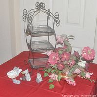 Wrought iron three tier display shelf with 3 glass inserts, 4 stone animal figurines, and brass planter with artificial flowers on red tablecloth.