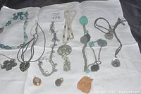 Overview of 9 necklaces and 3 pendants arranged on white fabric background showing colors, materials, and styles.