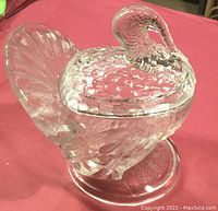 Photo shows clear pressed glass candy nut dish shaped as a turkey with detailed textured feathers, lid forming upper body and head with curved neck and head, round base.