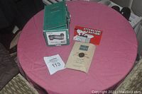 Figurine box, certificate, and caution note on pink round table with tour paper tag numbered 113