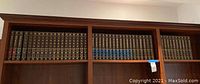 Wide view of Britannica encyclopedia collection on wooden shelves showing dark hardcover books arranged in order.