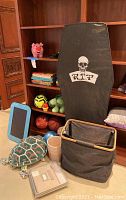 Photo shows assorted kids toys and balls, a black coffin-shaped item with R.I.P skull design, books on shelves including a pink pig stuffed animal on top shelf.