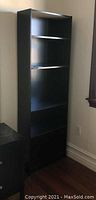 Full view of tall black wooden bookshelf with five compartments, standing upright in a room corner.