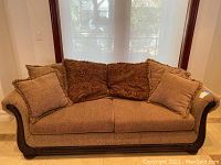 Front view of the brown upholstered couch with pillows, showing the fabric texture and wooden trim.