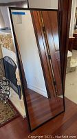 Full-length floor mirror standing upright showing the black frame and clear reflection.