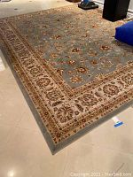 Full view of rectangular wool area rug laid on tile floor showing blue field and ivory border