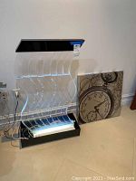 Front view of the decorative water fountain with flowing water on acrylic panels illuminated by LED light, next to the stacked square wall art canvas with clock design.